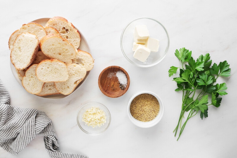 Ingredients for vegan garlic bread: sliced Italian bread, vegan butter, garlic, vegan Parmesan cheese, salt, and black pepper.