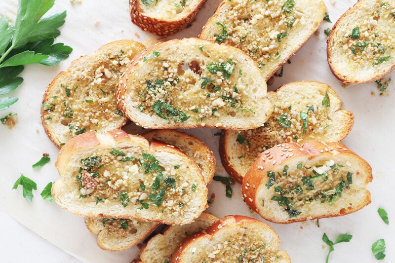 Vegan garlic bread, sprinkled with vegan Parmesan and fresh parsley on parchment paper.