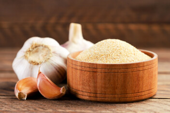 Ground garlic in a bowl and fresh cloves on a wooden background