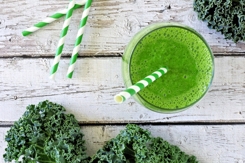 A glass of green kale juice with a paper straw.