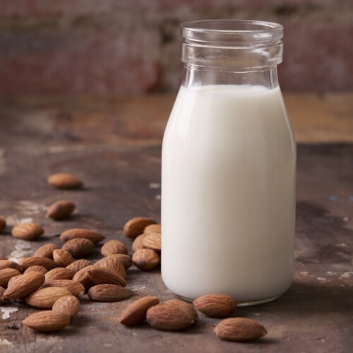 Homemade almond milk in a glass bottle with scattered almonds.