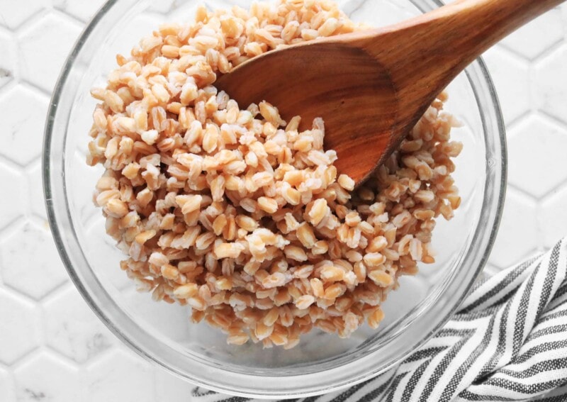 Cooked farro in a glass bowl with a wooden spoon