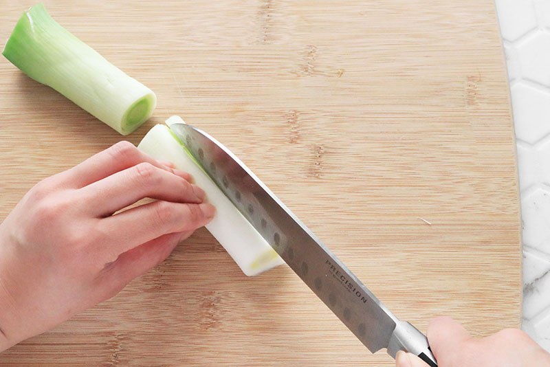 Woman's hand cutting a leek in half lengthwise