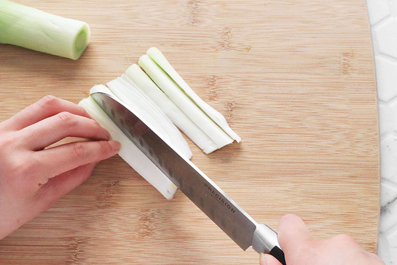 Woman's hand cutting a leek lengthwise on a cutting board
