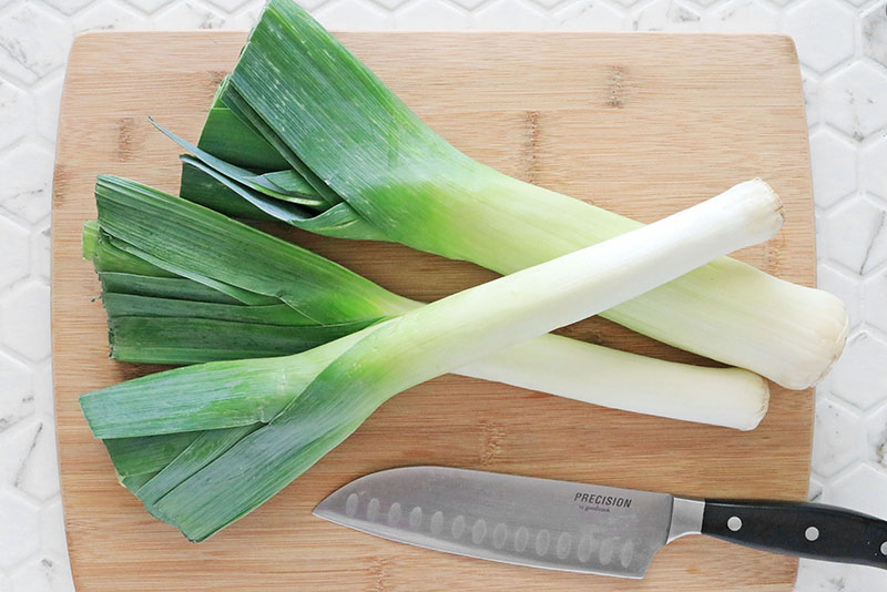 Three leeks on a bamboo cutting board with a chef's knife