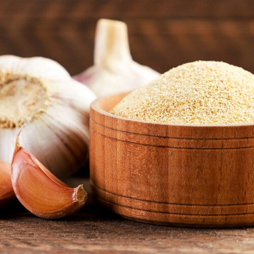 Ground garlic in a bowl and fresh cloves on a wooden background