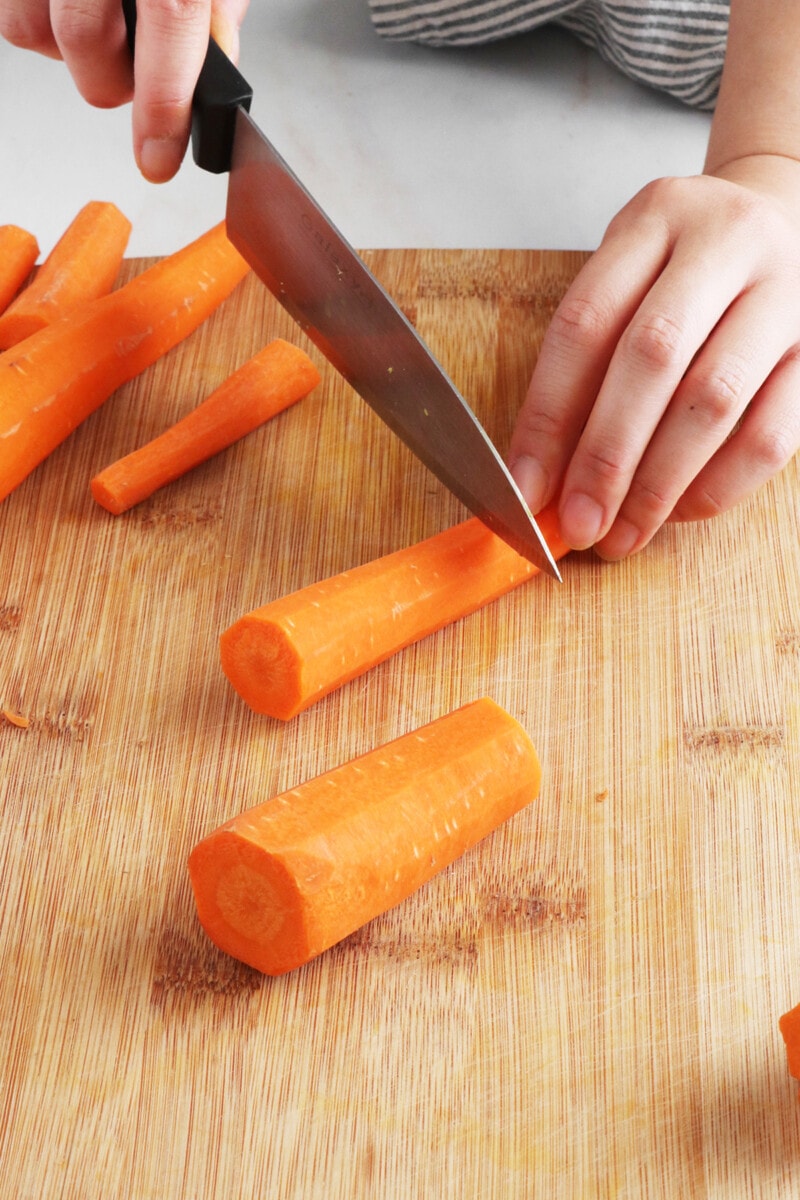 Cutting peeled carrots into 2-inch pieces on a cutting board.