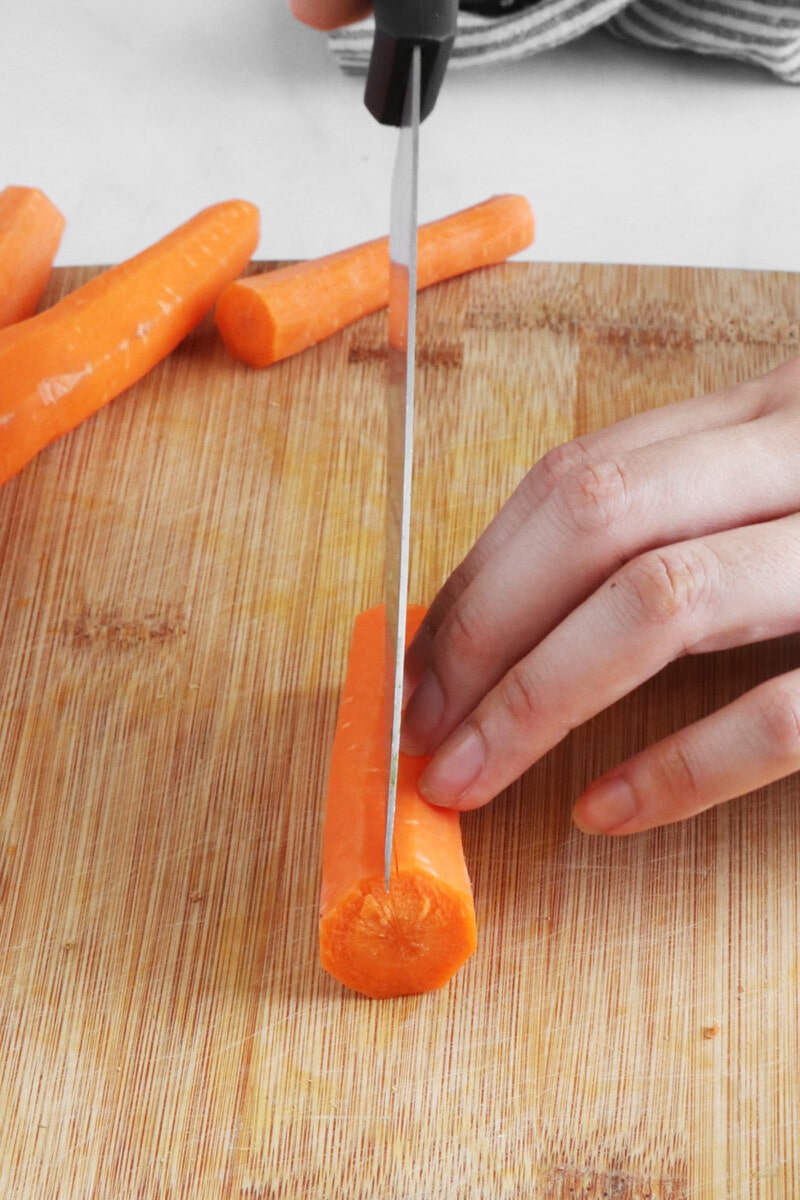 Slicing carrots in half lengthwise on a wooden cutting board.