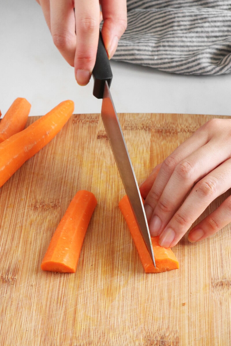 Slicing carrot halves into strips on a cutting board.