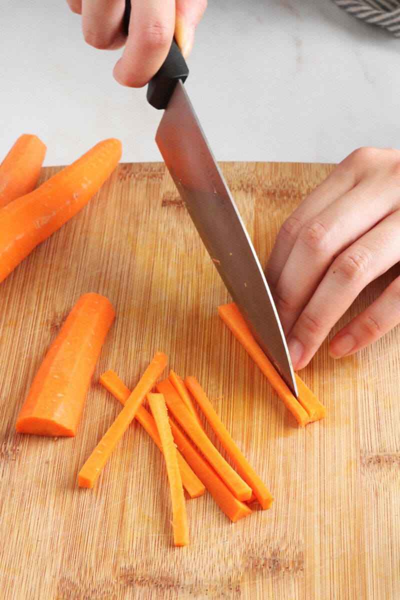 Slicing carrots into thin strips on a cutting board.