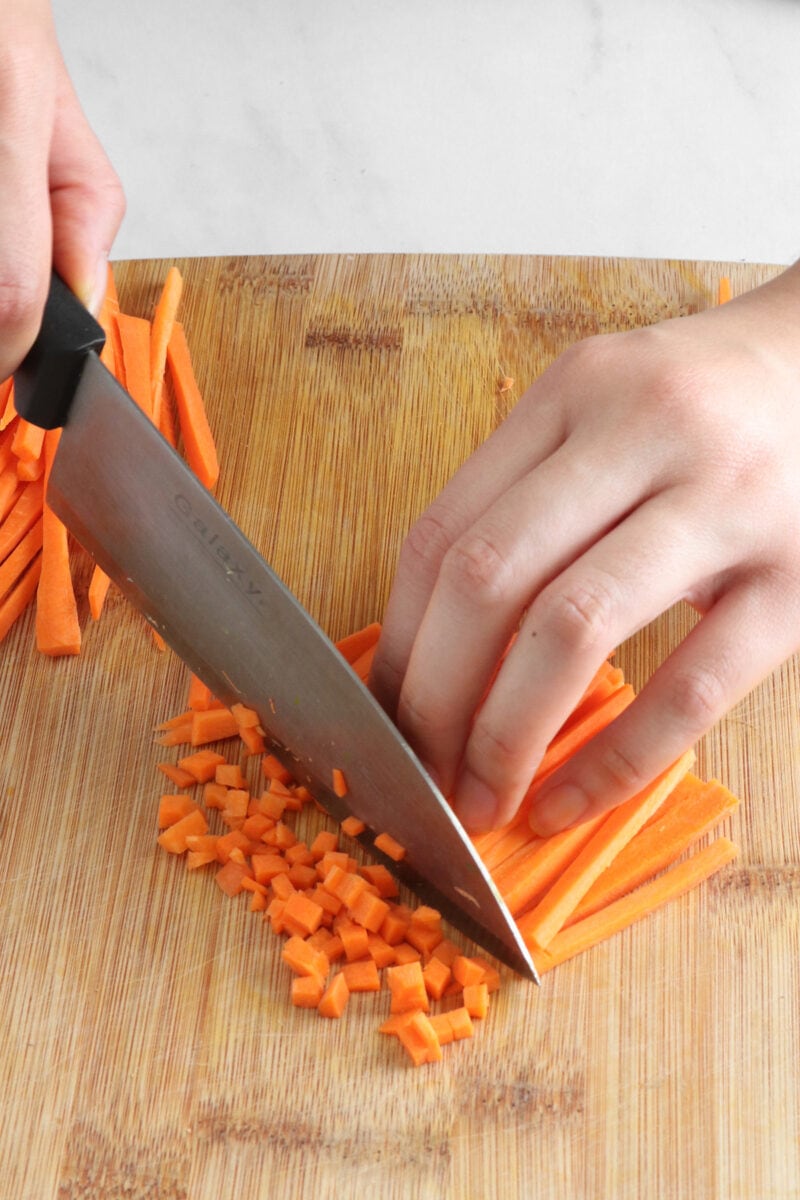 Chopping carrot strips into small cubes on a cutting board.