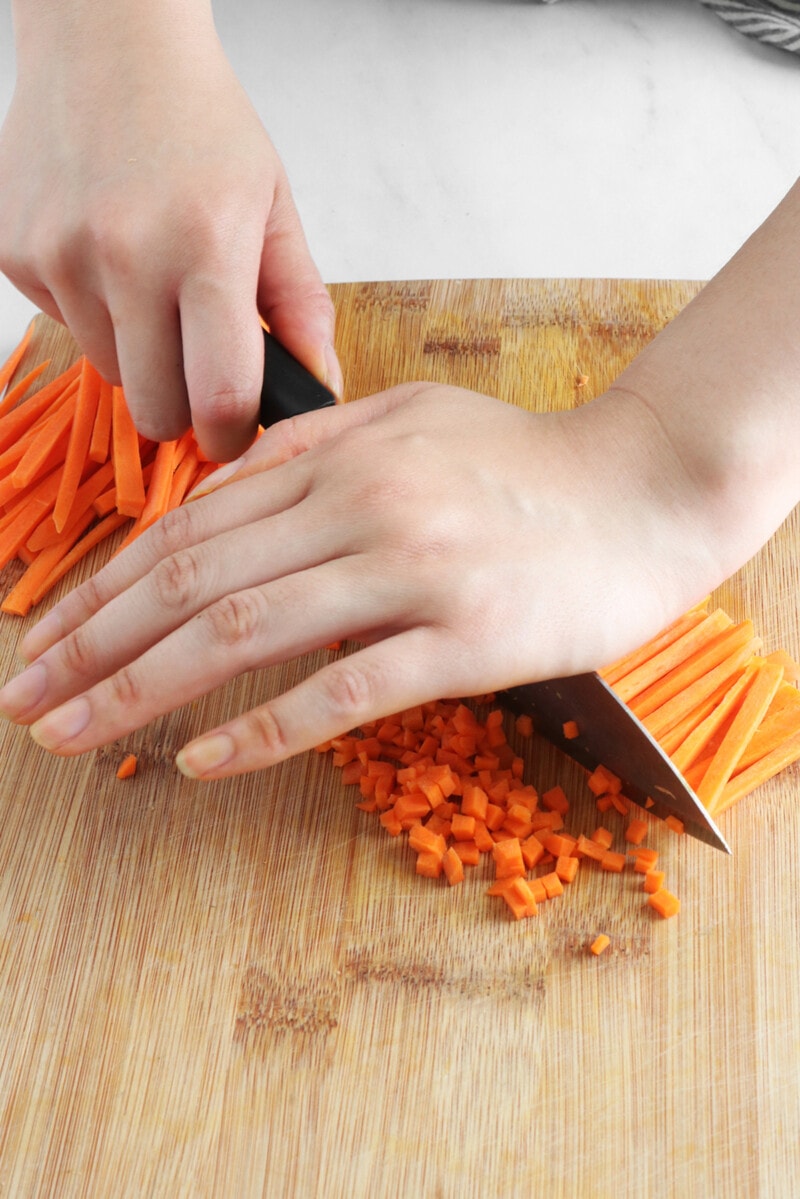 Using the palm of hand on the back of a knife to mince carrots.
