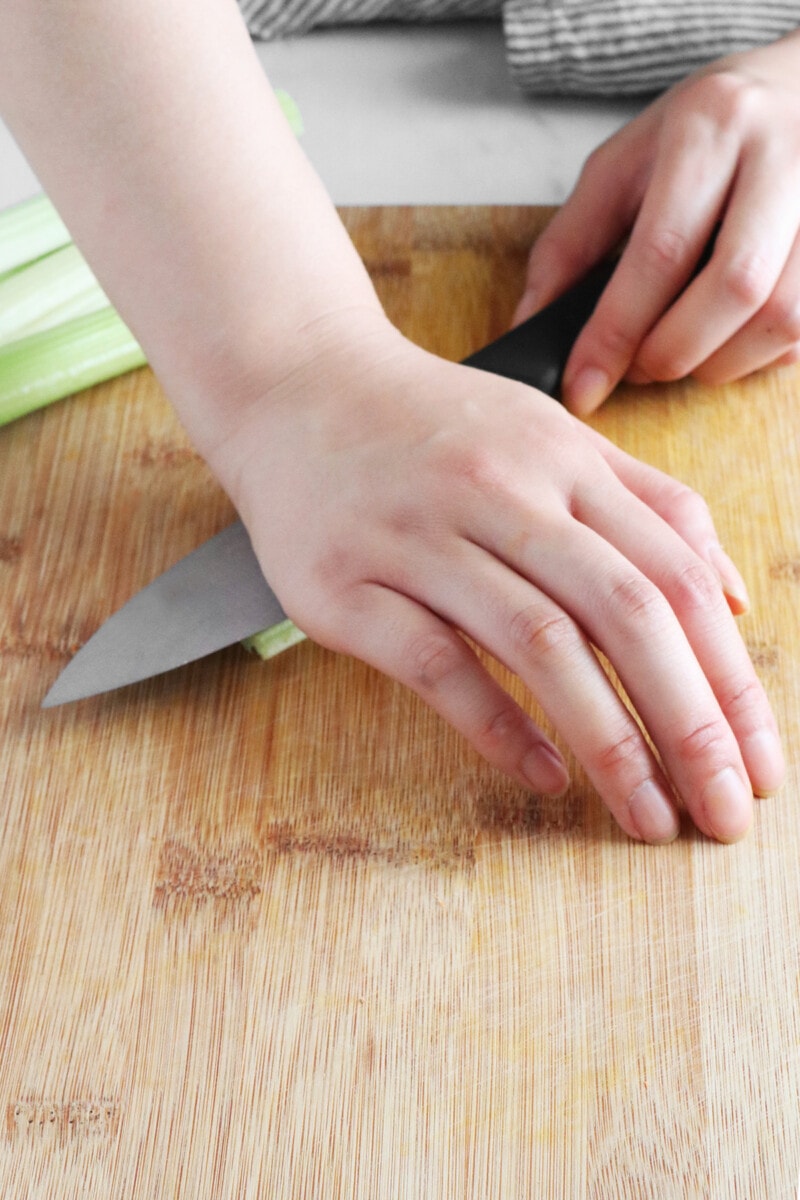 Using the palm of hand on the flat side of knife to press on top of the celery.