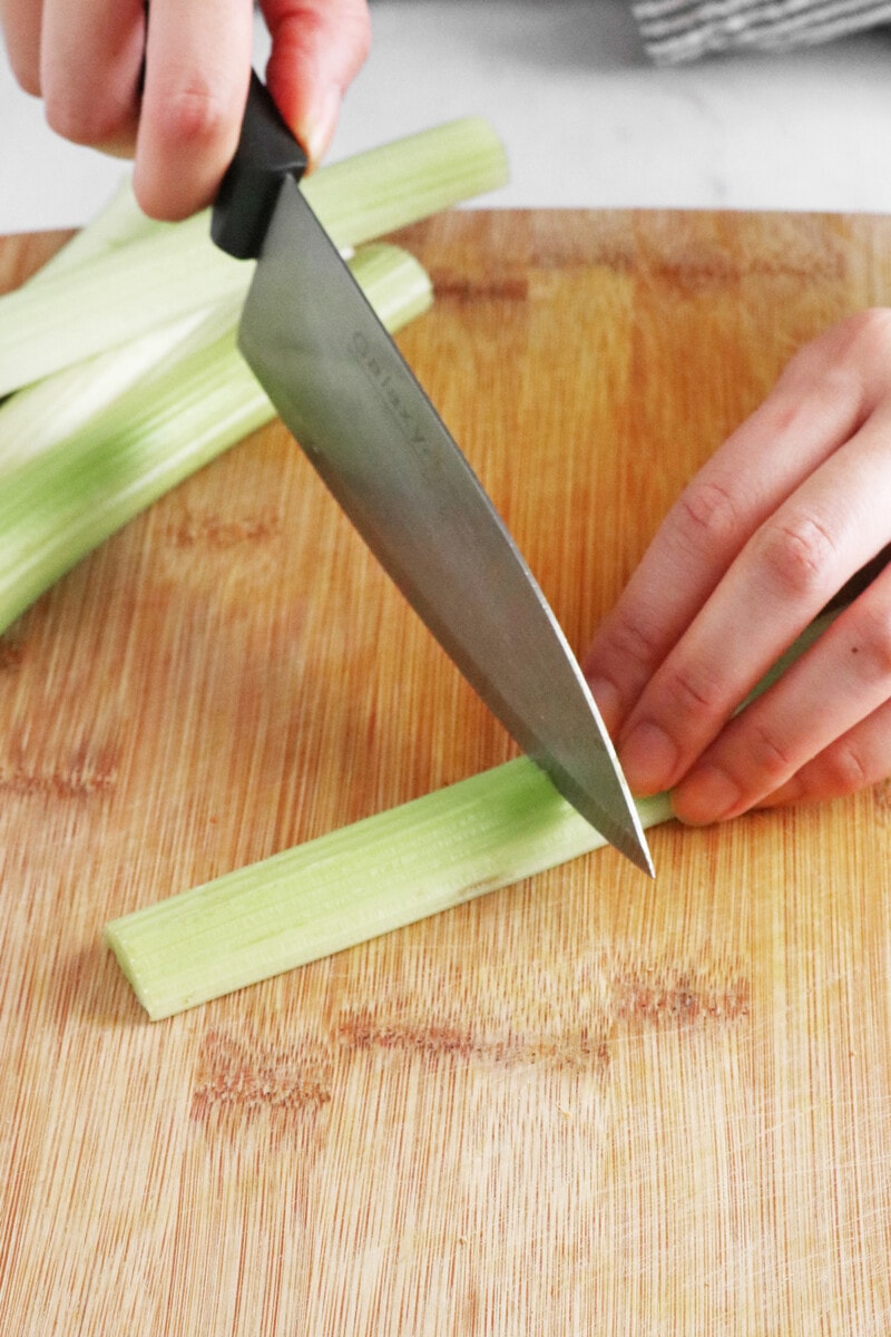 Chopping celery into 2-inch pieces on a wooden cutting board.