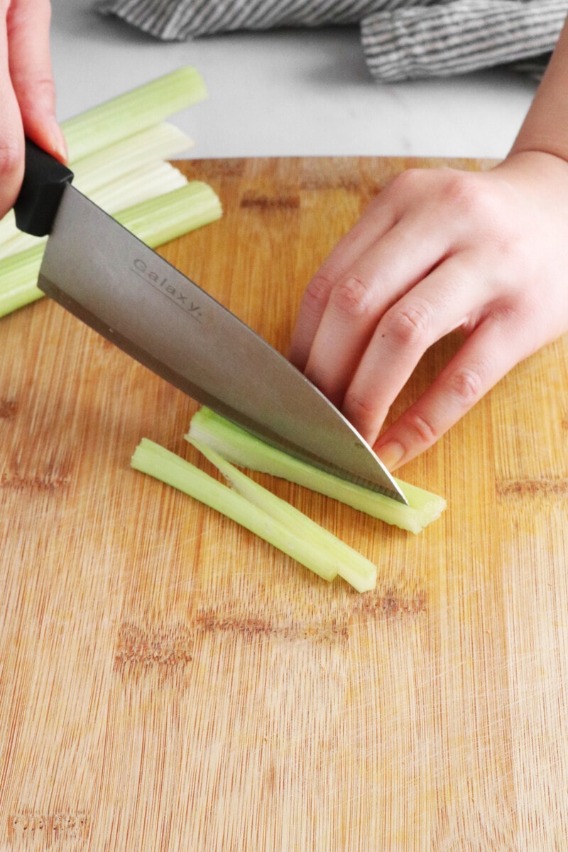 Slicing celery on a wooden cutting board.