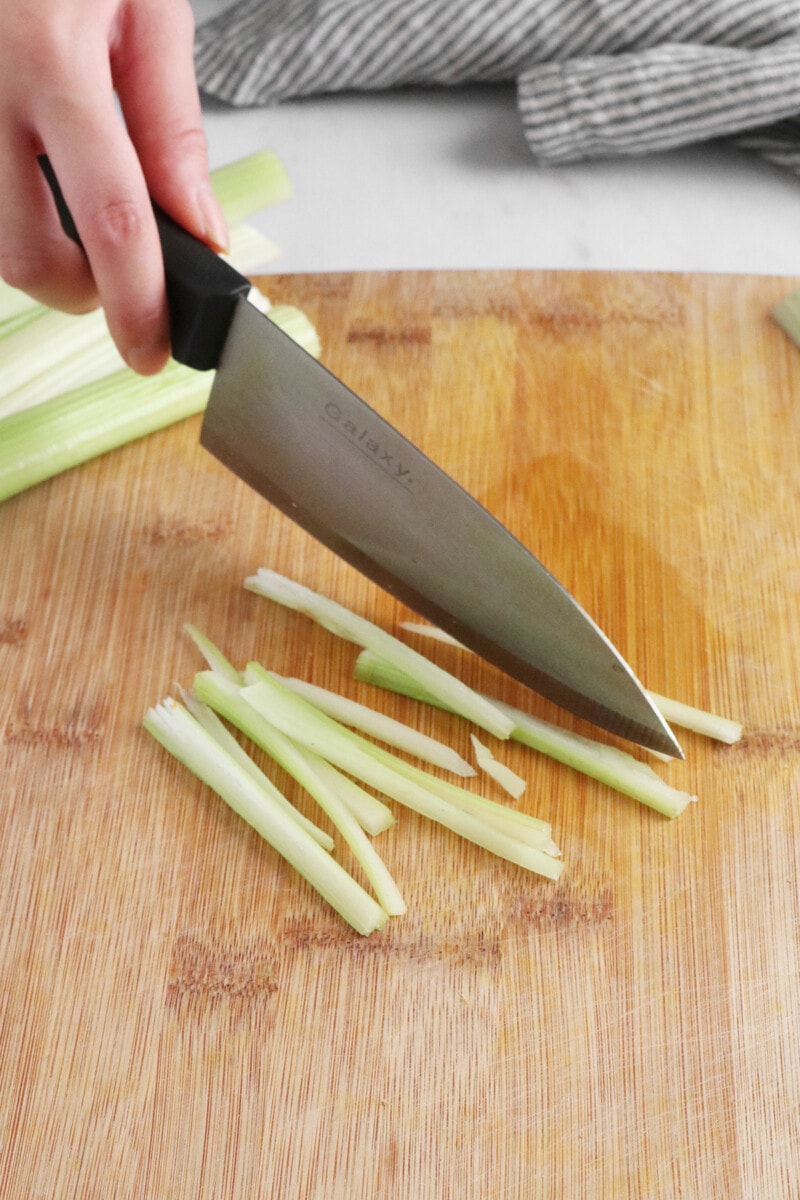 Slicing celery into thin strips on a wooden cutting board.