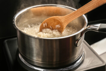 White rice reheating in a pot on the stove, with a wooden spoon stiring.