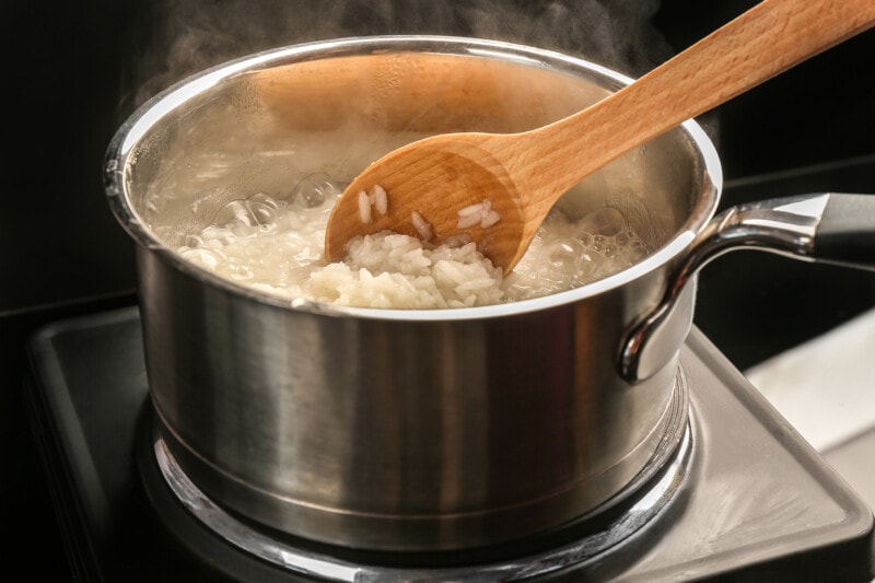 White rice reheating in a pot on the stove, with a wooden spoon stiring.