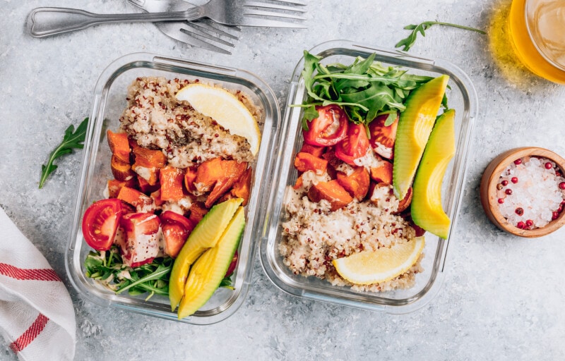 Affordable vegan meal prep containers filled with quinoa, tomatoes, avocado, and greens.