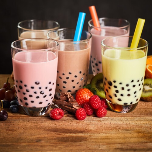 A row of different flavors of boba tea in clear glasses.