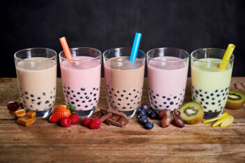 A row of different flavors of boba tea in clear glasses.