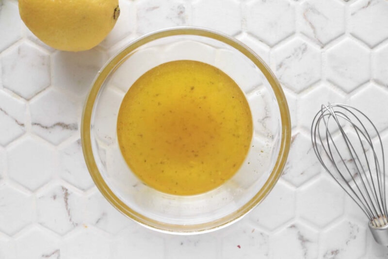 Whisking lemon vinaigrette ingredients in a glass bowl