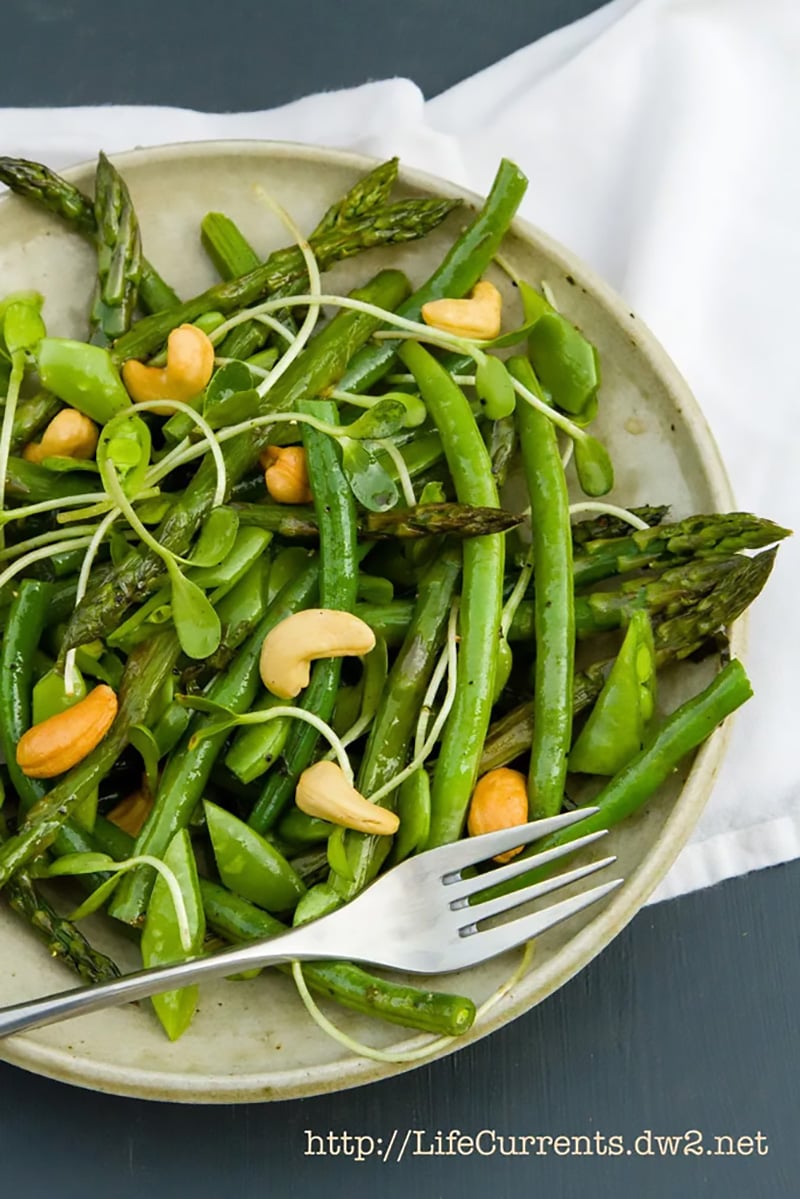 Asparagus spring salad topped with cashews and sprouts on a plate.