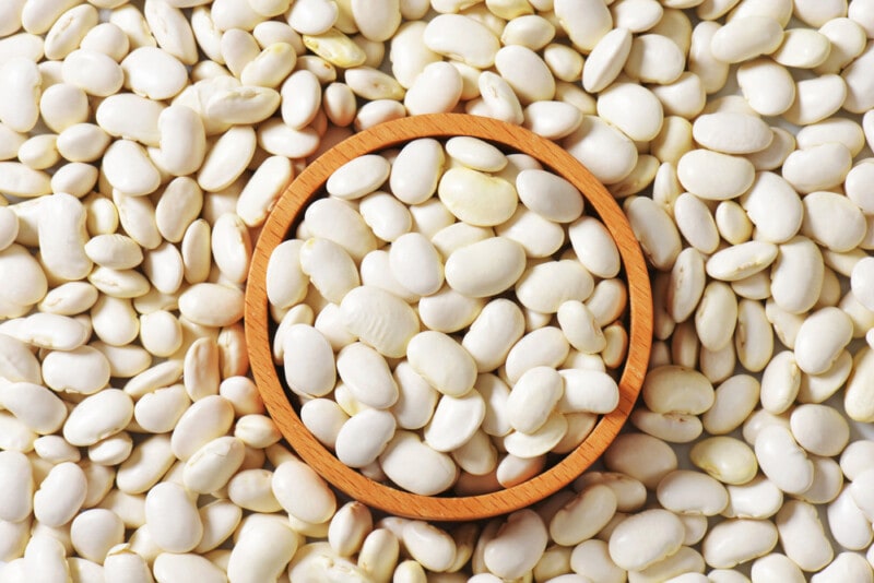 White Lima Beans surrounding and inside of a wooden bowl