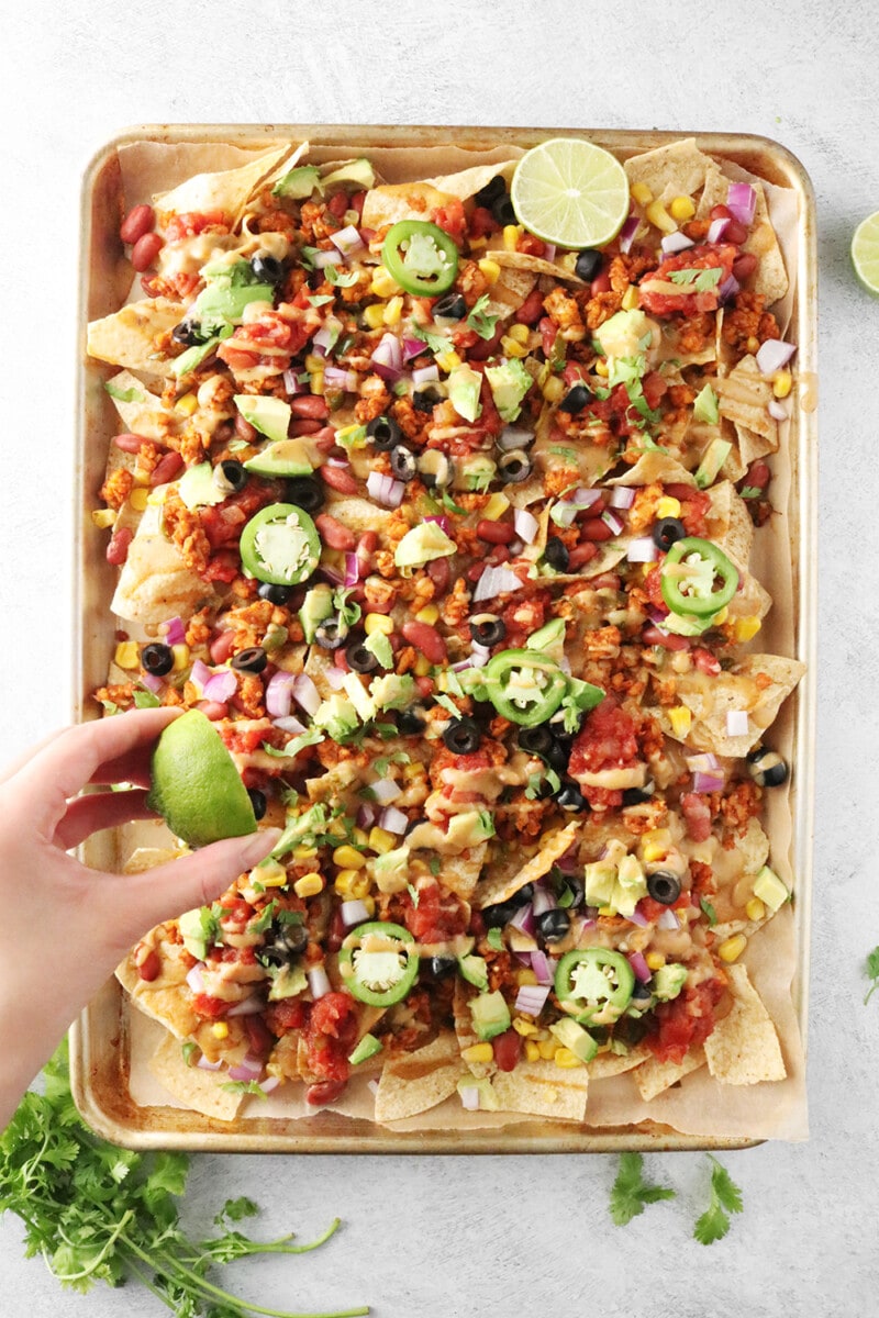 hand squeezing lime juice on Loaded Vegan Nachos
