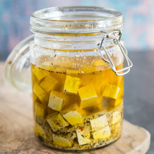 Raw tofu cubes marinating in a glass jar.