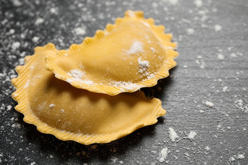 Fresh, uncooked Mezzelune pasta on grey wooden table, closeup.