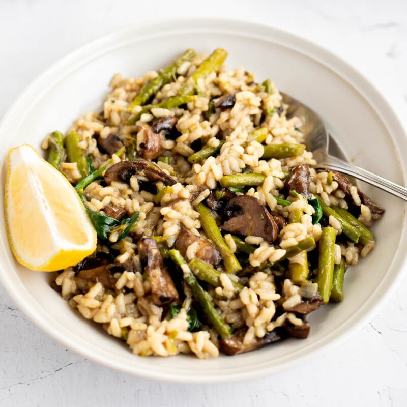 Close-up view of Mushroom and Asparagus Risotto in a white bowl with a lemon slice.