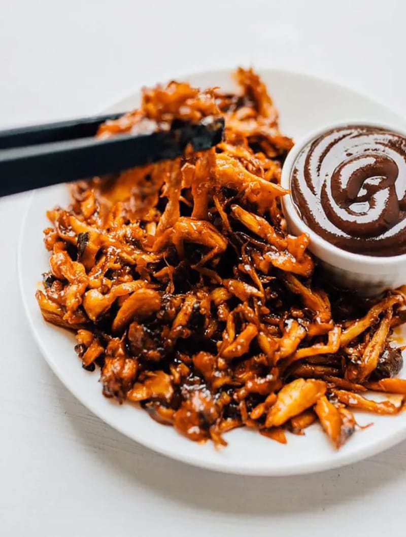 Vegan mushroom pulled pork on a plate, served with a dish of barbecue sauce.