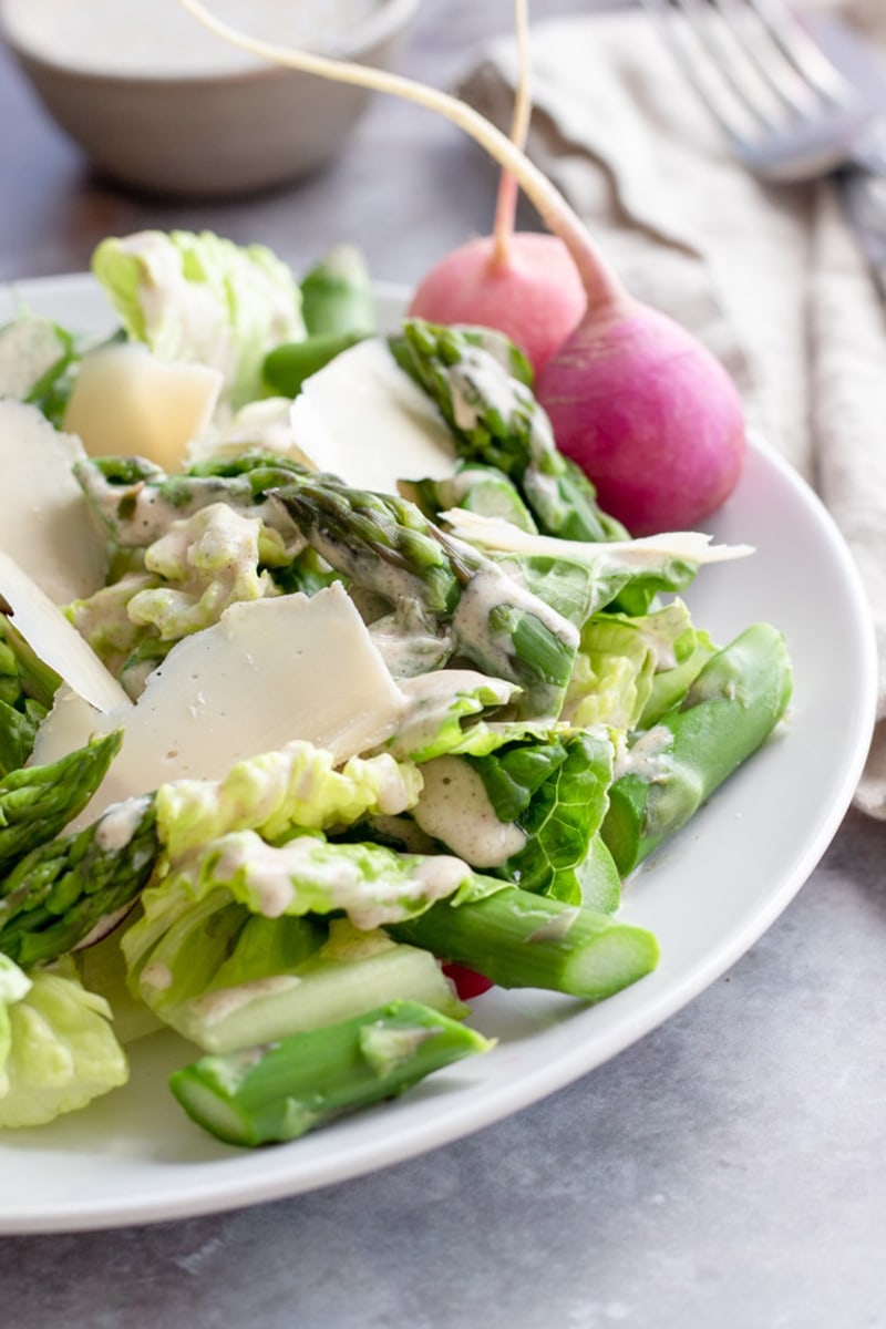 Asparagus salad and greens tossed in lemon chia dressing on a plate.