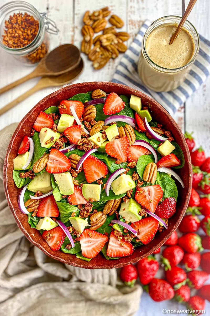 Fresh spinach salad topped with strawberries, avocados, and pecans in a bowl.