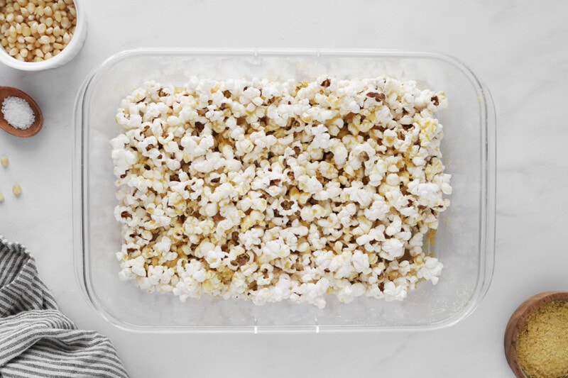 Mixing popcorn with nutritional yeast and salt in a large baking dish.
