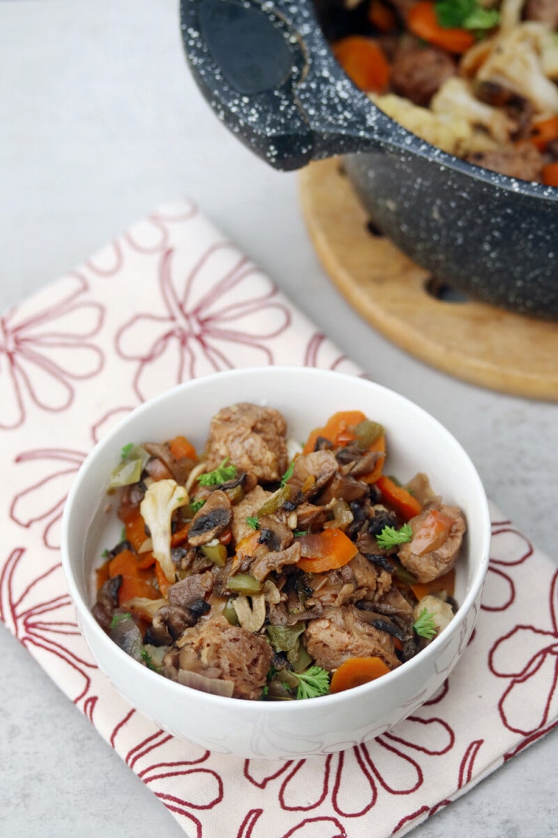 A warm bowl of vegan mushroom stew with carrots, cauliflower, soya chunks, and fresh herbs.