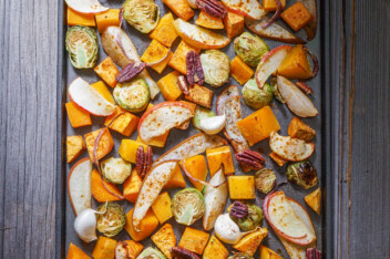 Roasted vegetables on a baking sheet: sweet potato, butternut squash, brussels sprouts, apple, pecans and pear.