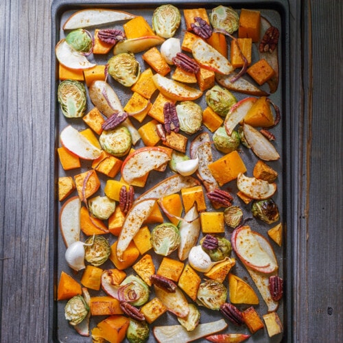 Roasted vegetables on a baking sheet: sweet potato, butternut squash, brussels sprouts, apple, pecans and pear.