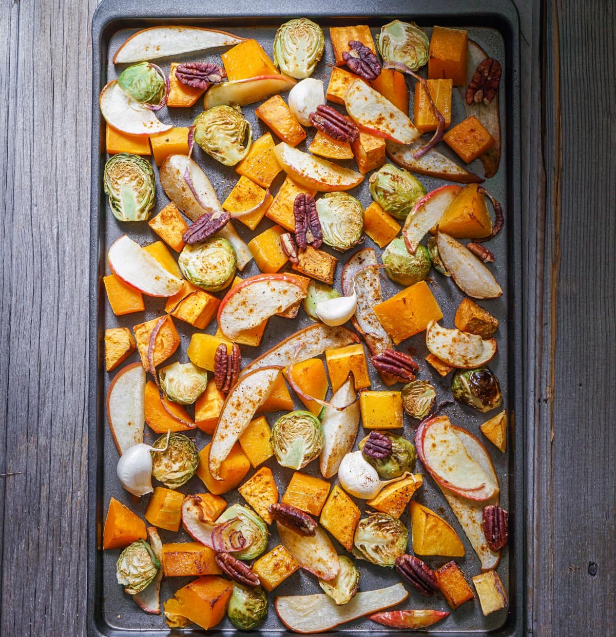 Roasted vegetables on a baking sheet: sweet potato, butternut squash, brussels sprouts, apple, pecans and pear.
