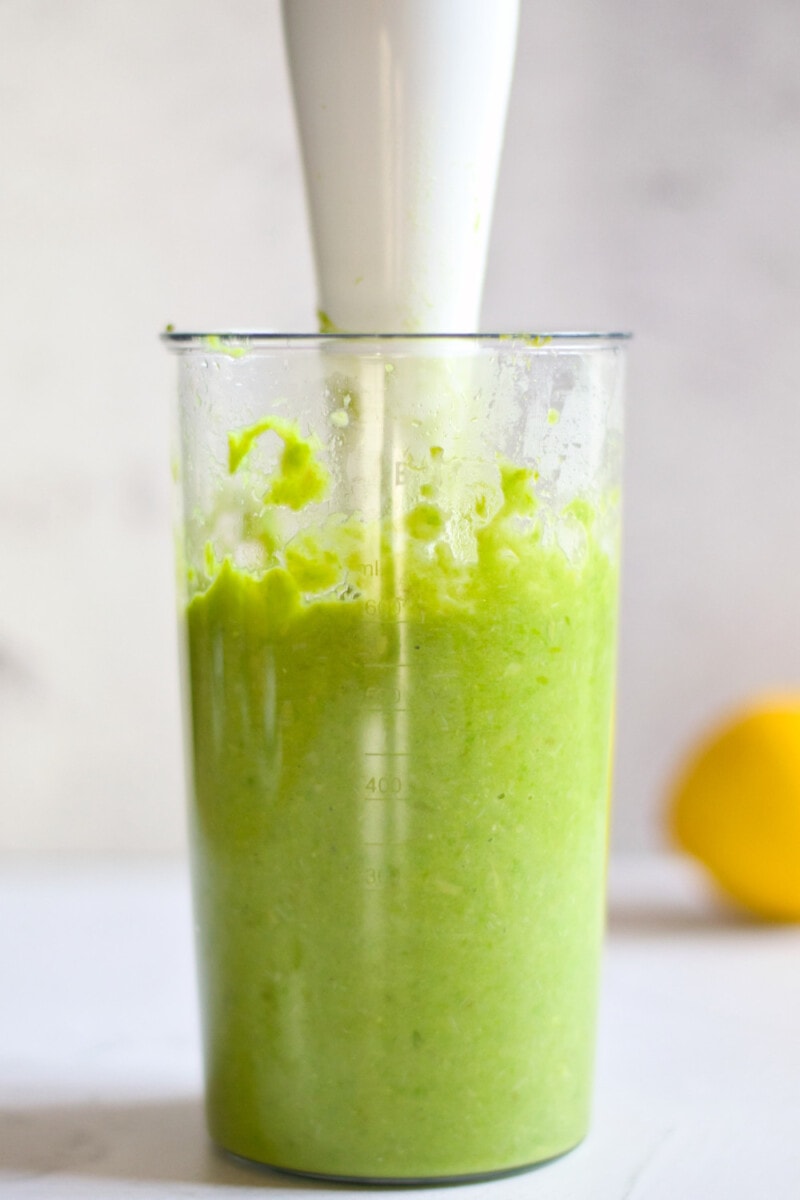 Pea and asparagus mixture in a cup with an immersion blender.
