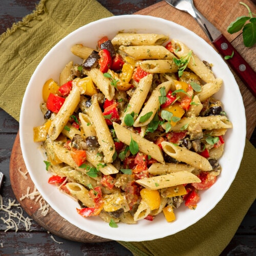 A bowl of vegan penne pasta with bell peppers and fresh herbs.