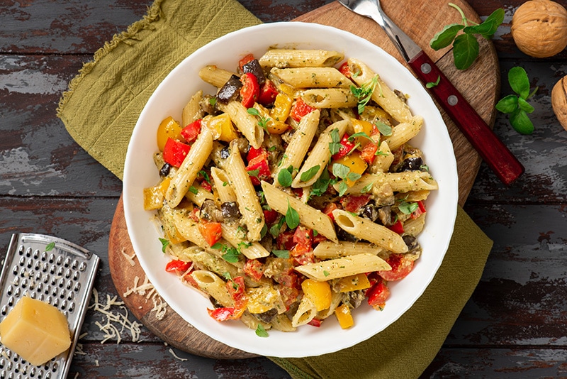 A bowl of vegan penne pasta with bell peppers and fresh herbs.