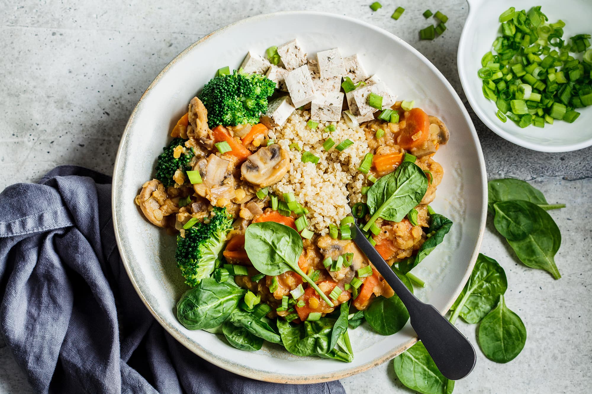 Vegan lentil stew with mushrooms, quinoa, spinach, and broccoli in bowl.