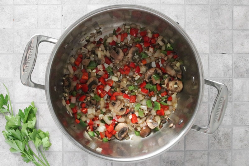 peppers, onions, and mushrooms sautéing in a large pot