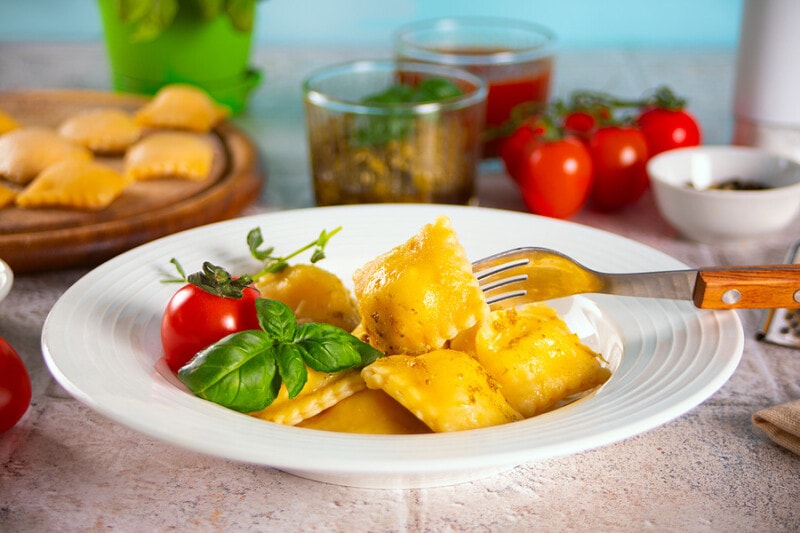 Ravioli pasta with fresh basil and tomato cherry on a white dish.