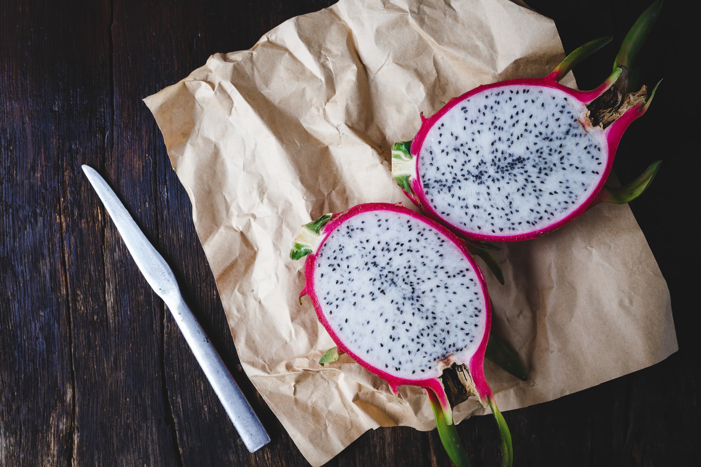 Ripe Dragon Fruit cut in half on a wooden table.