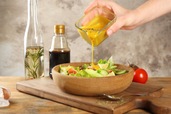pouring honey mustard salad dressing from a container onto a salad