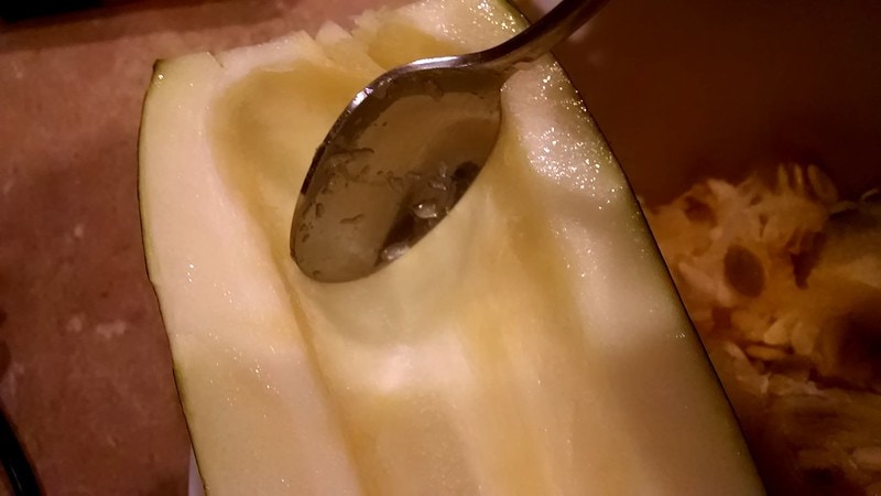 Using a spoon to scrape out seeds from a large zucchini