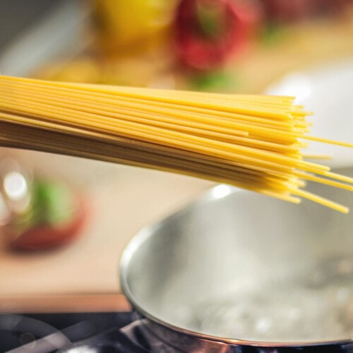 Hand holding uncooked spaghetti over a pot of boiling water.